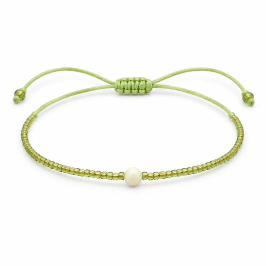 Jasnozielona cienka bransoletka boho z kremowym koralikiem, produkt na bialym tle